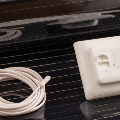 Un termostato y un cable junto a una película calefactora.