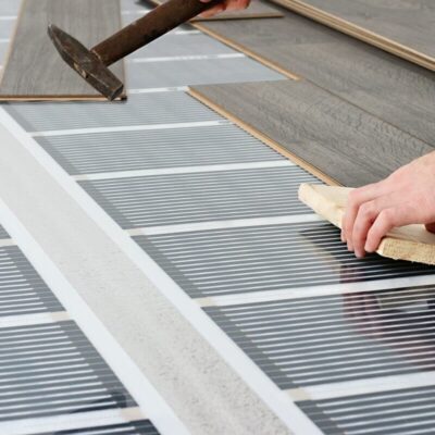Manos instalando película para paneles bajo un suelo laminado.