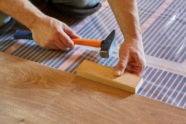 Manos instalando un suelo de madera sobre un folio radiante.