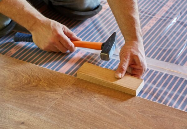 Manos instalando un suelo de madera sobre un folio radiante.