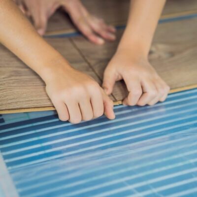 Manos instalando suelo laminado sobre calefacción por suelo radiante.