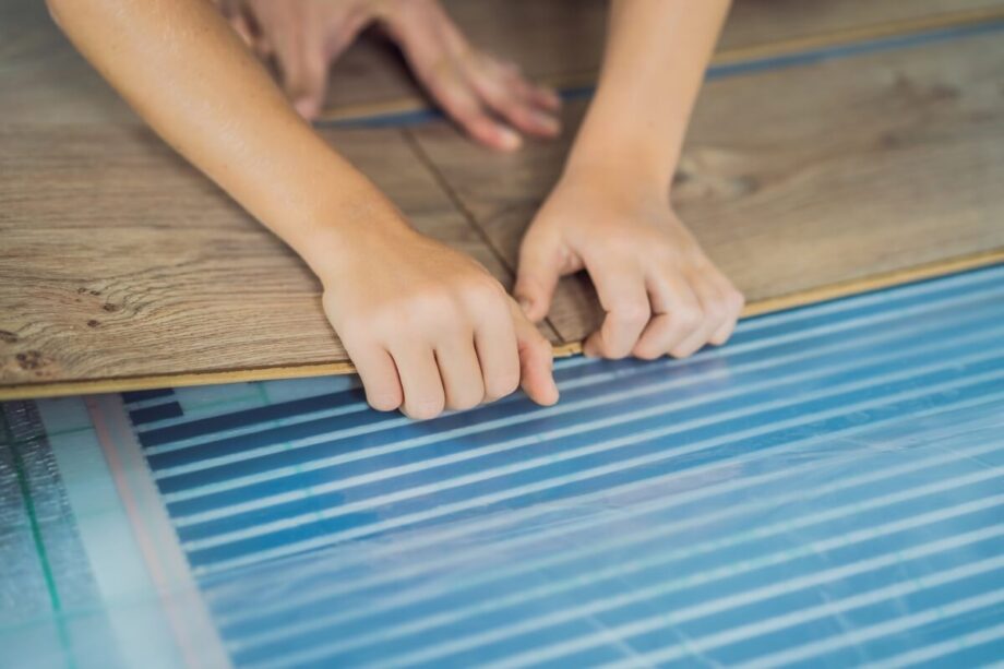Manos instalando suelo laminado sobre calefacción por suelo radiante.